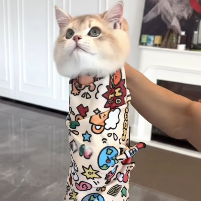 Cat wearing a colorful medical gown with cartoon designs, held by a person.