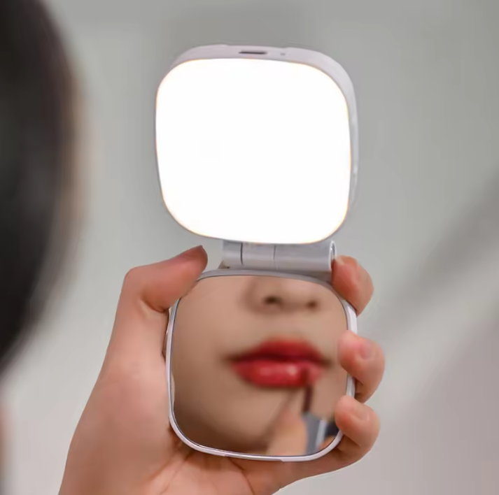 Hand holding a compact mirror with a light on a neutral background